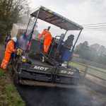Machine resurfacing on country lane with fields behind